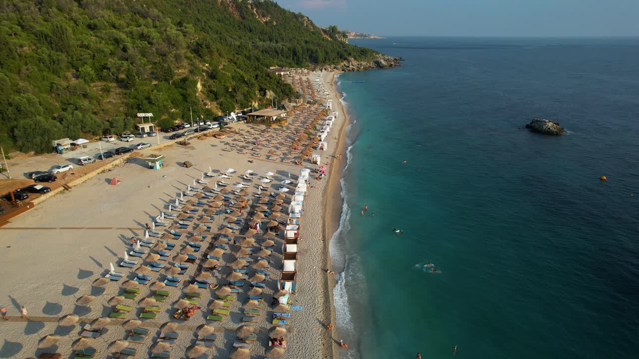 Tourists sunbathing on a beautiful beach with white sand, surrounded by green hills and crystal blue Mediterranean water