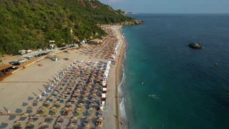 tourists sunbathing on a beautiful beach with white sand, surrounded by green hills and crystal blue mediterranean water