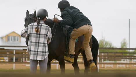 homem negro montando cavalo negro enquanto jovem segura a porta