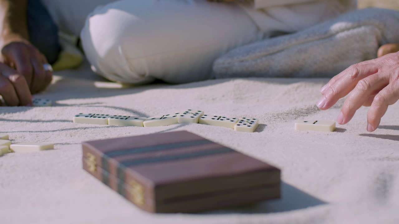 Senior people playing dominoes while sitting on blanket on shore