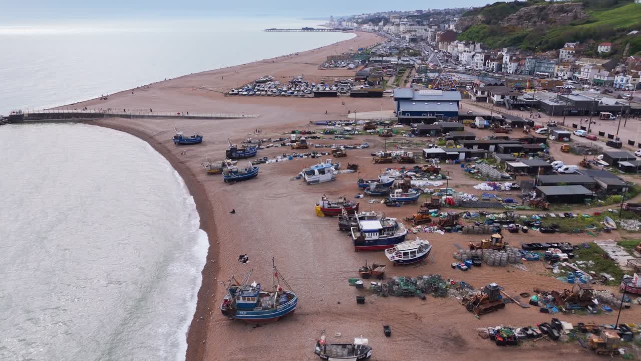 Aerial view of fishing boats and buildings scattered along Hastings beach. Coastal working life, rugged charm, and a vibrant fishing culture by the English Channel