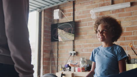 Happy-pre-teen-boy-shaking-hands-with-his-father-to-celebrate-finishing-the-build-of-a-racing-kart-in-their-garage,-close-up,-low-angle