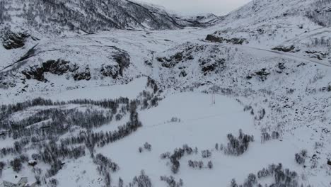 Drone-view-in-Tromso-area-in-winter-flying-over-a-snowy-landscape-with-wooden-houses-and-white-mountains-in-Norway