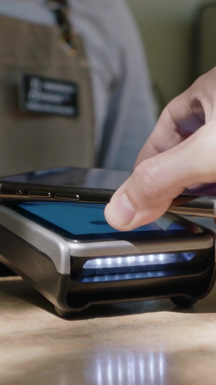 Vertical video: Hand entering customer paying cell on POS at cafe masked staff apron badge watching