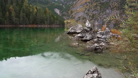 Revealing-view-from-the-middle-of-Blindsee,-an-alpine-lake-in-autumn-with-clouds-obscuring-the-mountains-if-the-alps