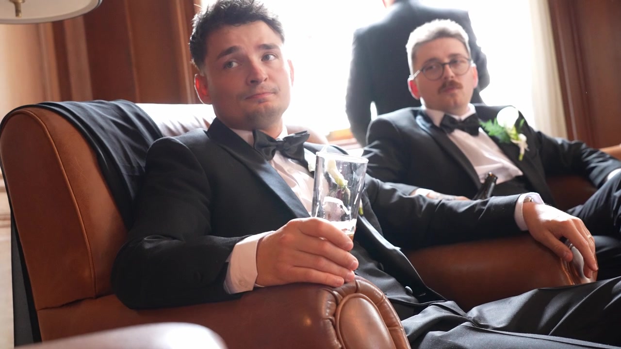Due uomini vestiti elegantemente si rilassano con un drink in un interno raffinato, prima di una celebrazione o un evento formale. Concetti di amicizia, tempo libero, matrimoni, lusso e incontri sociali.
