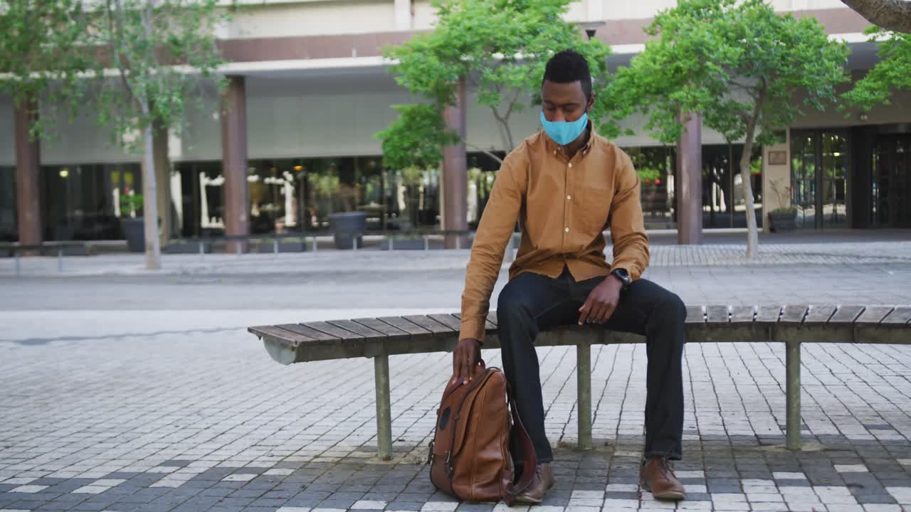 벤치 에 앉아 있는 얼굴 마스크 를 착용 한 아프리카계 미국인 사업가