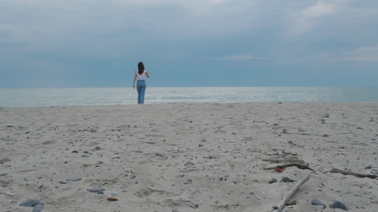 Close up of a woman walking away from the camera on the cloudy beach in Prince Edward County, Ontario, Canada