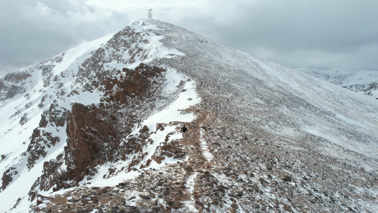 вид с воздуха на одинокого мужчину, бегущего под горной вершиной с вышкой сотовой связи в холодный зимний день, съемка с дрона