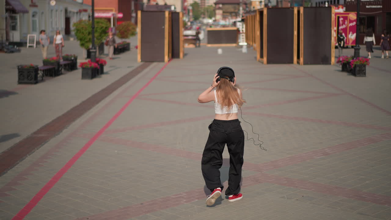 Ballerina di strada bianca che esegue un freestyle sicuro di sé in una piazza illuminata dal sole, pantaloni larghi e scarpe da ginnastica rosse, braccia e piedi espressivi, atmosfera da coreografa, linee di pavimentazione urbana, piazza vuota, calda