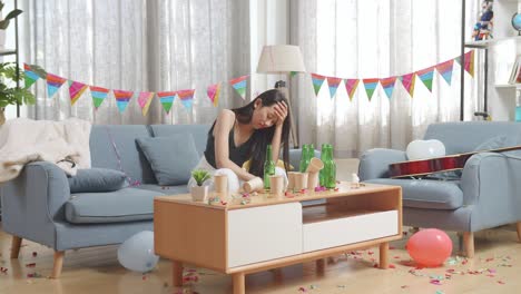 drunk asian woman sitting on a sofa and holding her head with hands after having a party at home