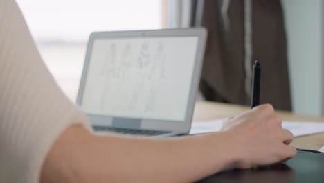 caucasian adult woman using laptop and mobile app and designing a dress.