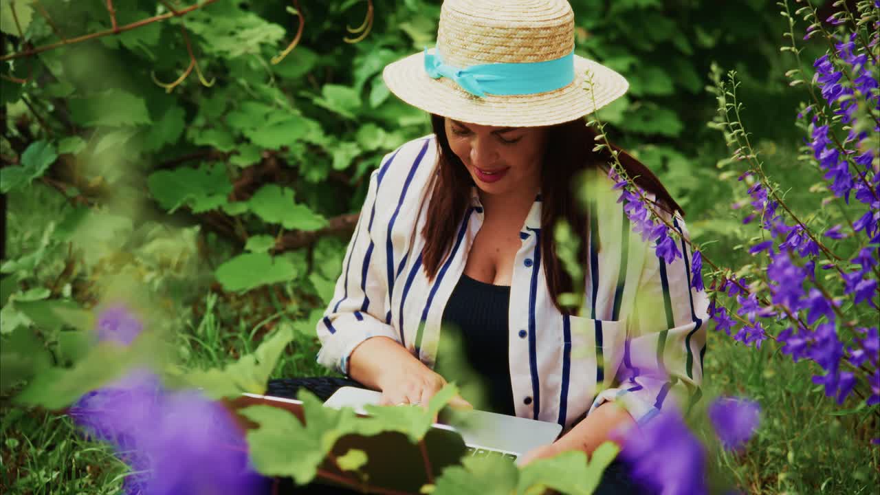 Woman in straw hat reading a book surrounded by vibrant flowers in a lush garden setting