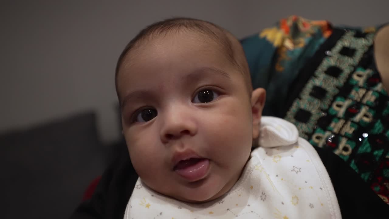 lindo bebé de dos meses siendo expresivo mientras su madre lo sostiene en el interior