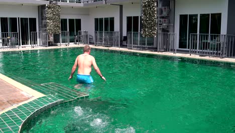 a man walks into the pool and swims