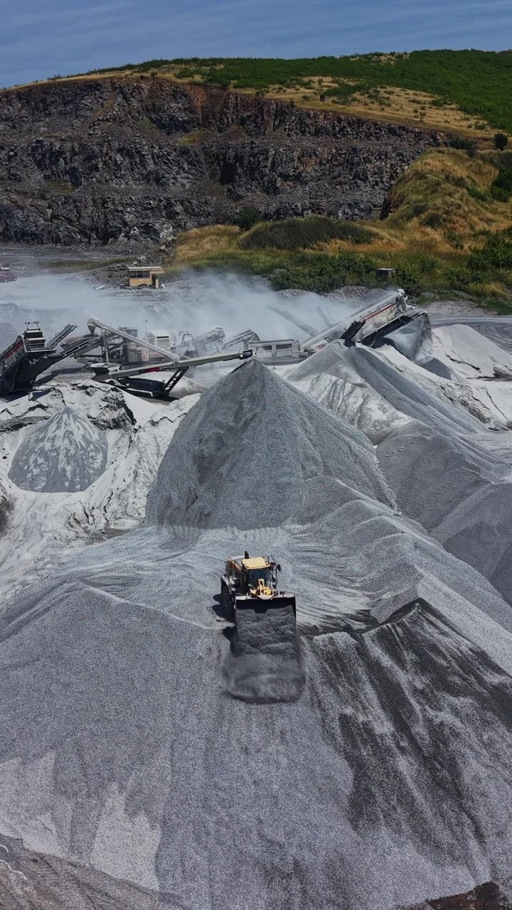 Heavy machinery moves materials at a gravel site near a hill