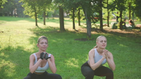 Zwei-Schöne-Blonde-Sportliche-Frauen,-Die-Im-Park-Kniebeugen-Machen