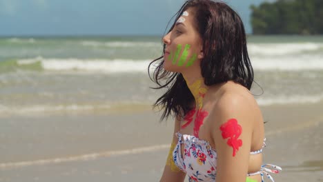a sunny caribbean day sees a girl in a bikini and body paint lounging on a white sand beach facial close up