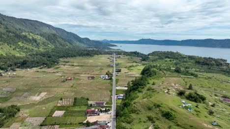 pulau samosir's long road with lake toba and lush landscapes in sumatra, indonesia, under a cloudy sky, aerial view