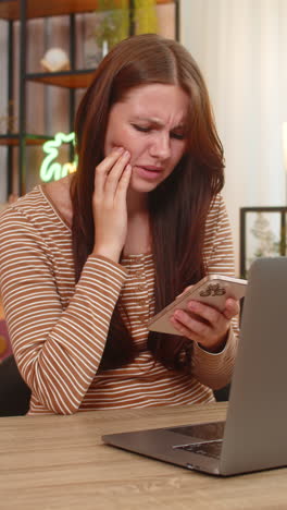 Young woman touches cheek feels tooth pain searches dentist contacts on smartphone and books online