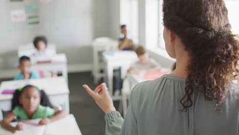 video de una maestra caucásica dirigiendo una lección en una clase de alumnos diversos