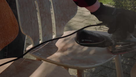 detail shot of handyman using polishing machine to polish wood and refurbish an old vintage design chair in the garden on a sunny day 4k