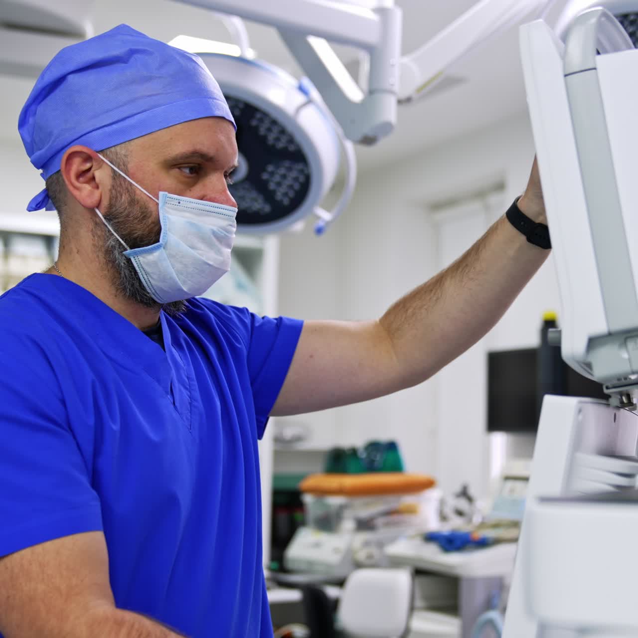 Male doctor in mask and blue uniform rotates the screens of lung ventilator machine. Medic getting ready for modern surgery