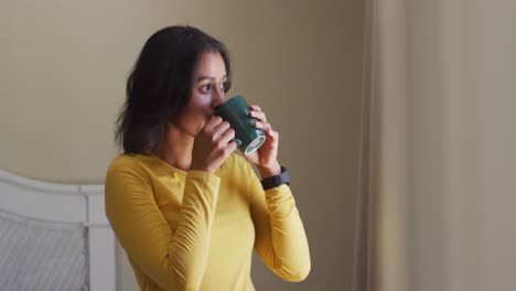 Relaxed-biracial-woman-drinking-coffee-and-looking-outside-window