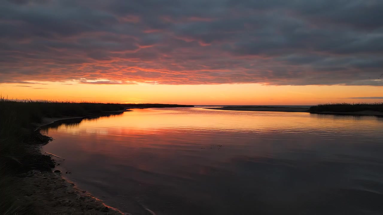 Solnedgang over roligt vand indrammet af silhuetter af marskgræs