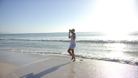 Young-biracial-woman-walks-along-the-shore,-shielding-her-eyes-from-the-sun-with-her-hand