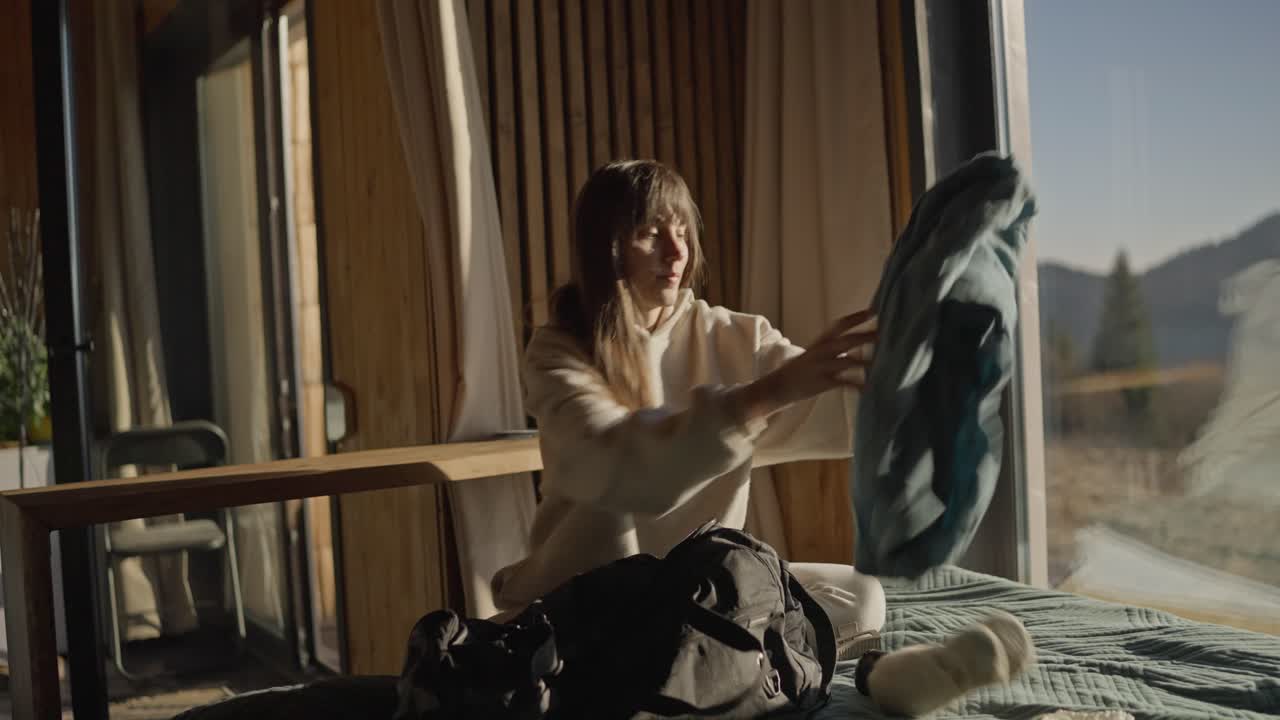 Woman packing a backpack in a cozy cabin with a mountain view