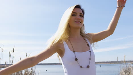 Beautiful-young-woman-having-fun-and-twirling-around,-lake-in-the-background