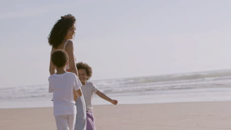 beautiful american woman walking with her two cute kids at seashore on bright sunny day