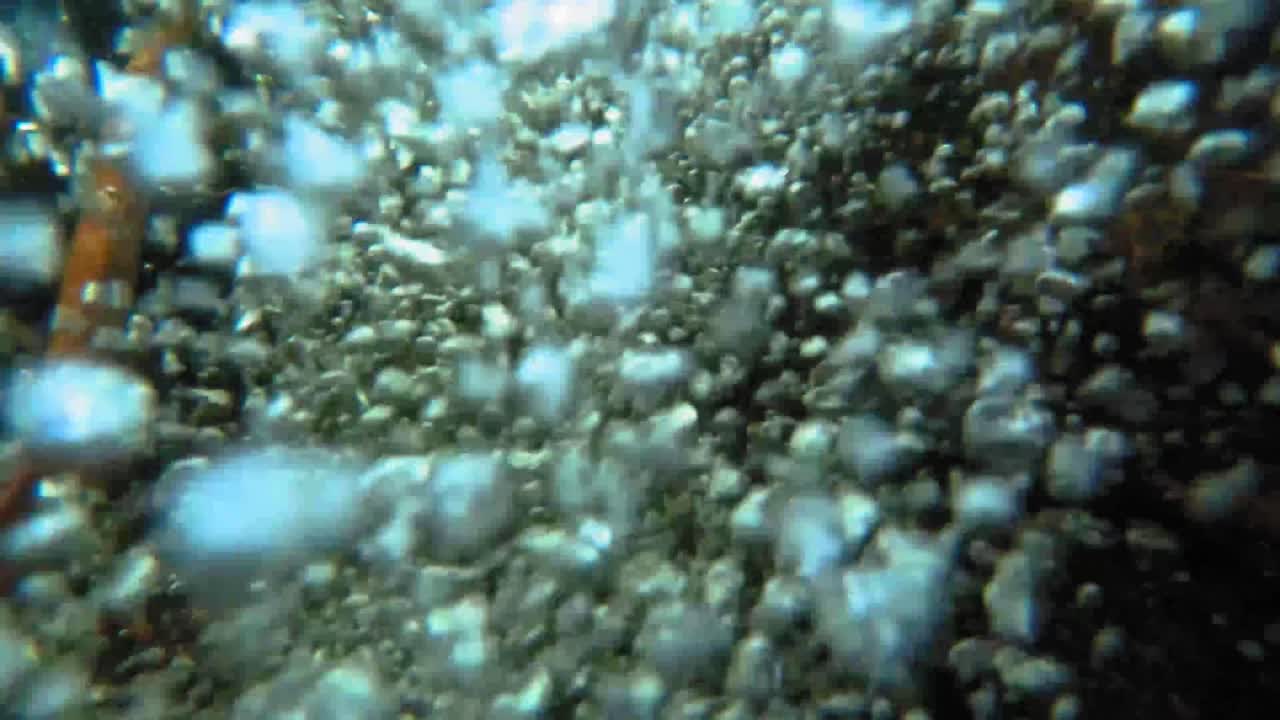 SLOW MOTION underwater close up of bubbles from a small waterfall in a forest stream