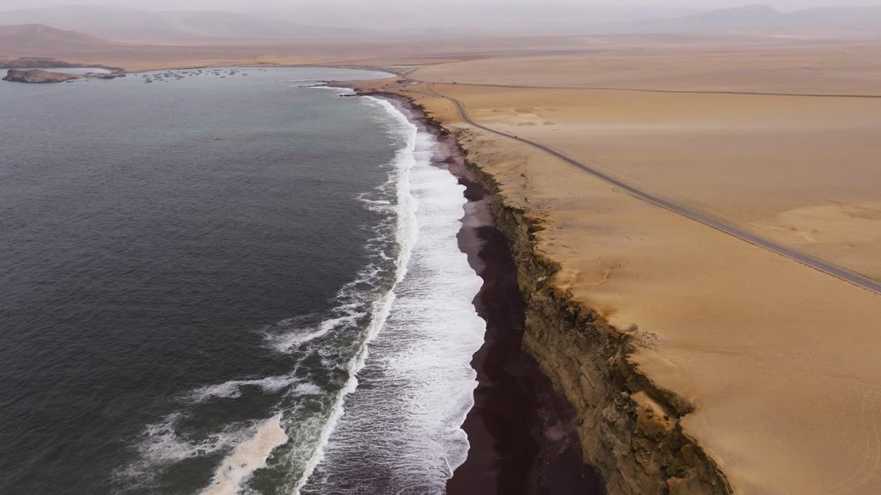 Pale sand narrows into a sweeping point where surf breaks rhythmically along the Paracas coast, aerial pullback as waves crash