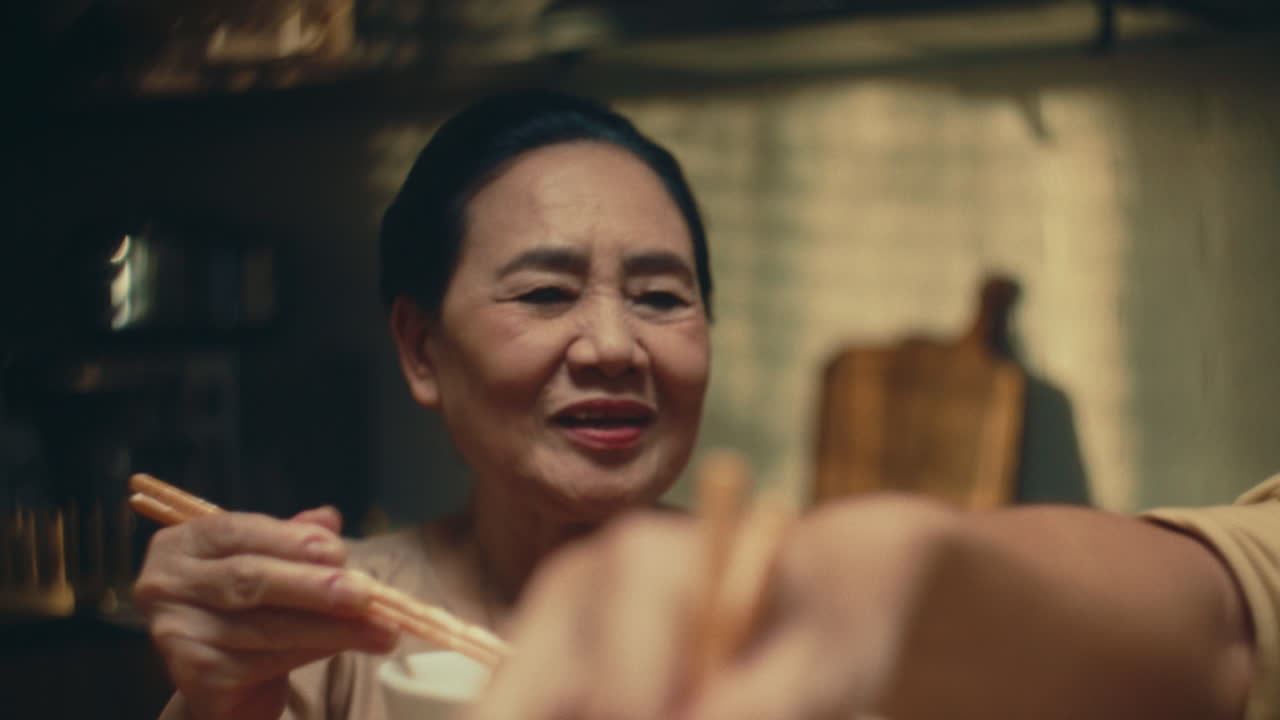Elderly Asian Woman Eating Dinner with Chopsticks