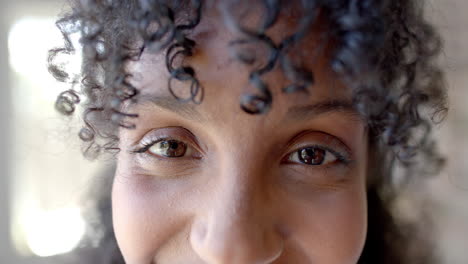 Portrait-of-happy-biracial-fitness-teenage-girl-with-curly-hair-in-white-room,-slow-motion