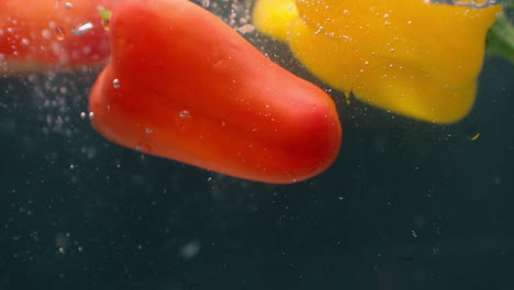 cerrar varias rebanadas cortadas de pimienta de campana verde y amarilla roja fresca arrojado y flotando en agua transparente clara bajo ángulo de vista lateral movimiento lento