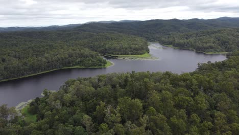 4k aerial view of water reservoir surrounded with thick green bushland