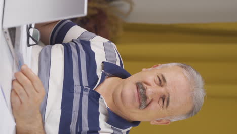 vertical video of home office worker old man scratches his ears looking at camera.