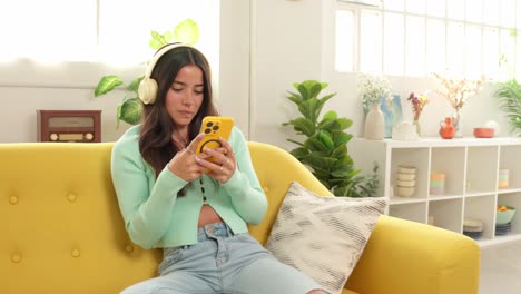 woman with headphones using phone on sofa