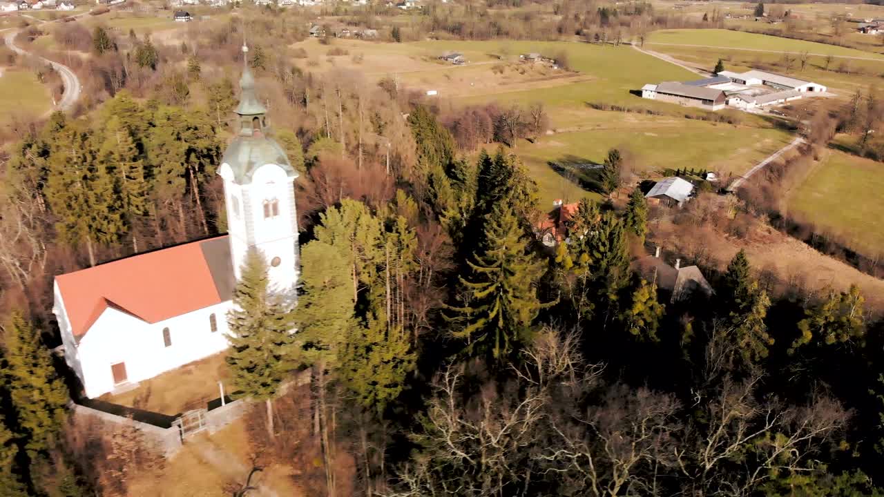 Aerial flight over a church nestled on a hill in Slovenia. Camera heading directly towards the Church looking down on the church.