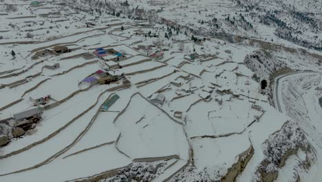 Vista-Aérea-De-Las-Tierras-De-Cultivo-De-La-Aldea-Rural-Cubiertas-De-Nieve-En-El-Valle-De-Naltar,-Gilgit