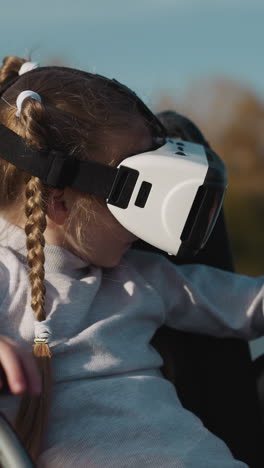 female kid with disability plays computer game using vr headset. preschooler girl moves head looking at new location on blurred background closeup