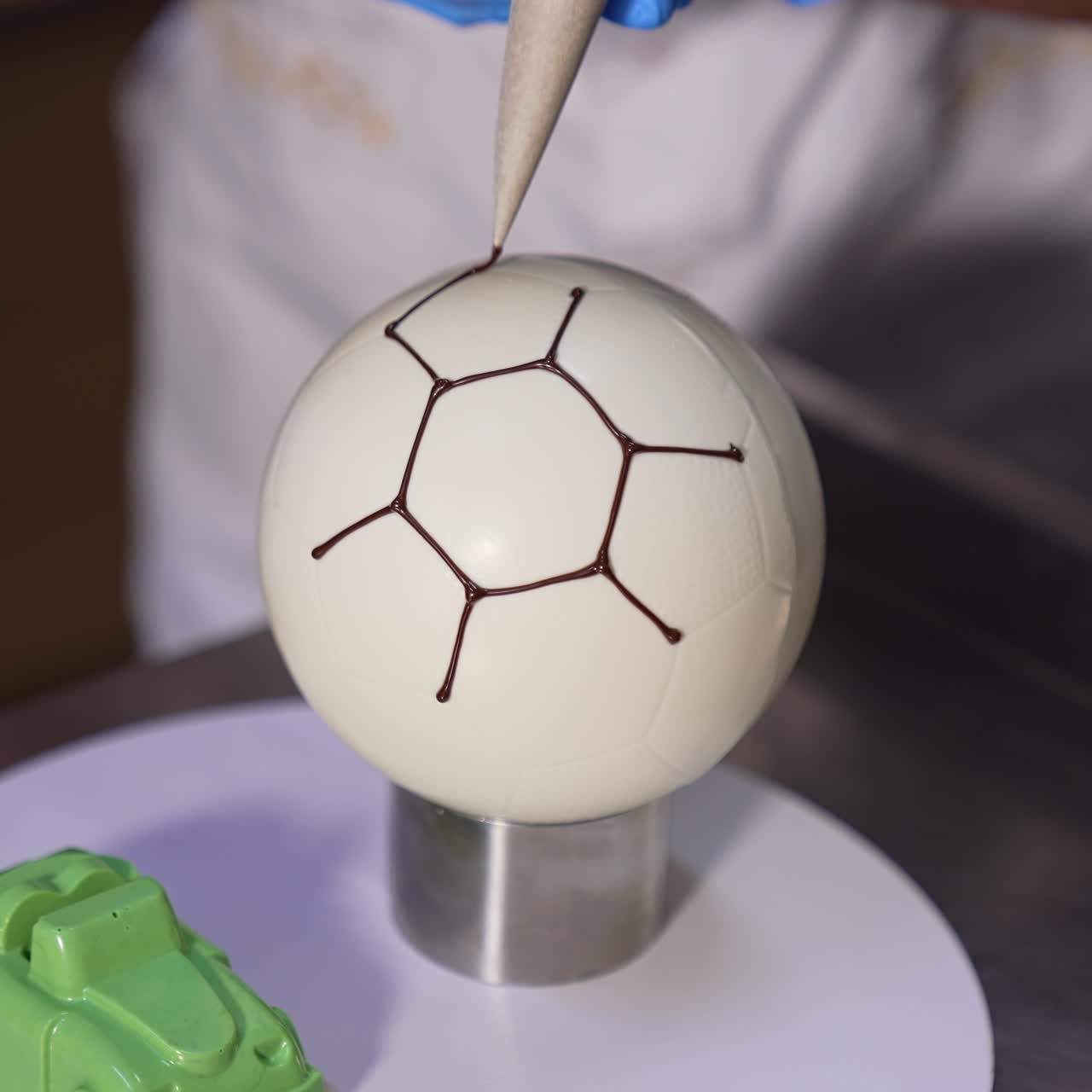 Confectioner decorates ball-shaped white cake with chocolate. Producing desserts at factory close up. Blurred backdrop