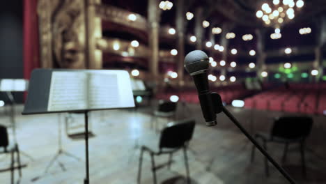 primer plano de un micrófono en un escenario con soportes de música y sillas