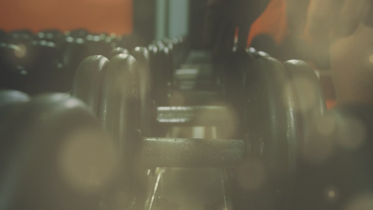 Hand entering frame and forearm hovering then gripping, sliding and extracting dumbbell for workout