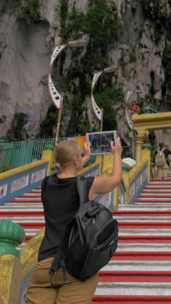 Donna turista che sale scale colorate e scatta foto con il tablet.