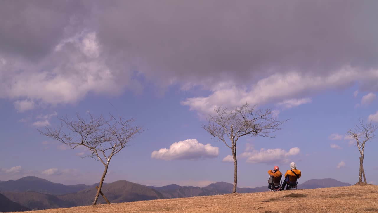 구름이 지나가는 산 정상에서 밖을 내다보는 의자에 앉아 있는 커플