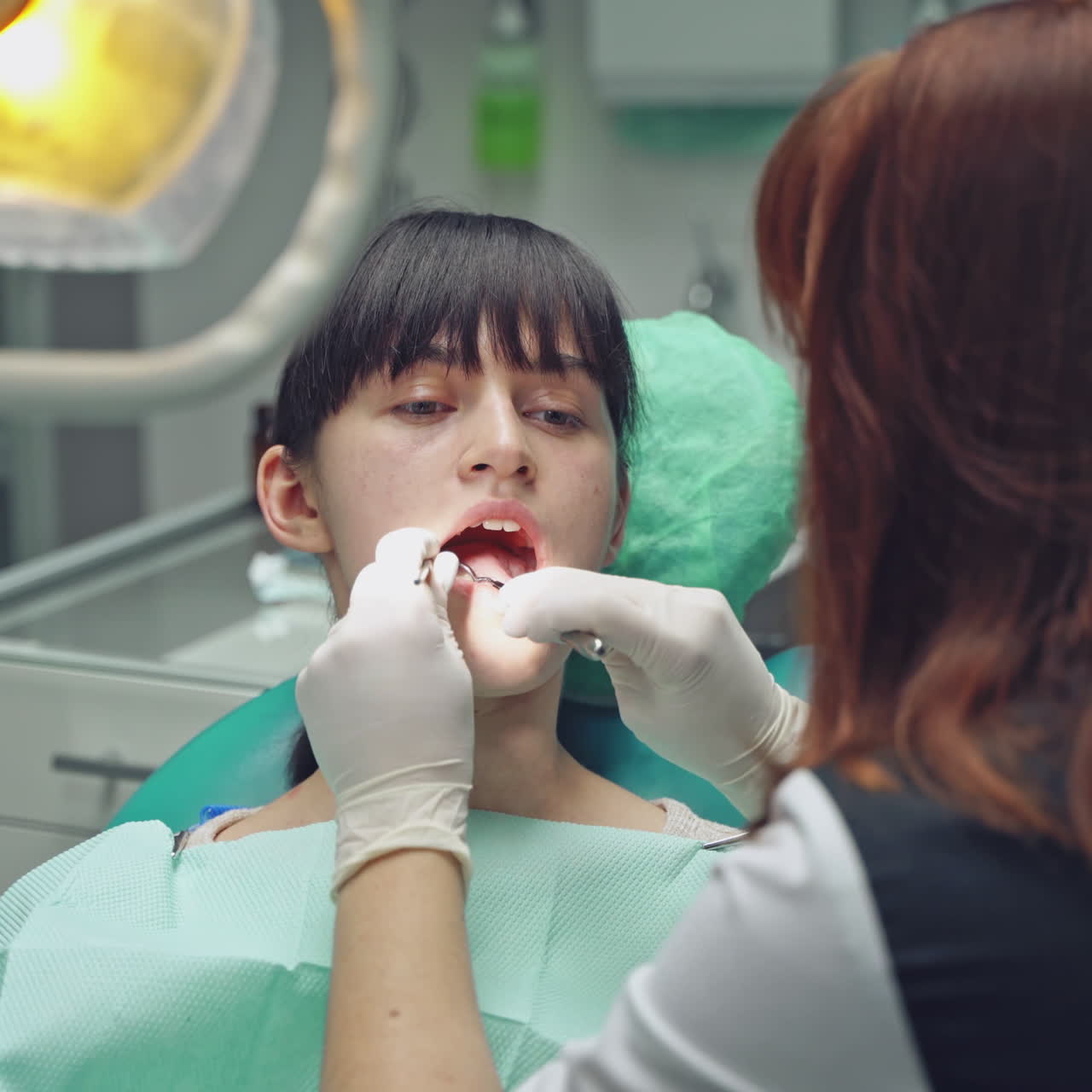 A dentist examines the oral cavity of a young client, who is sitting on the dental chair in the office. Close-up.